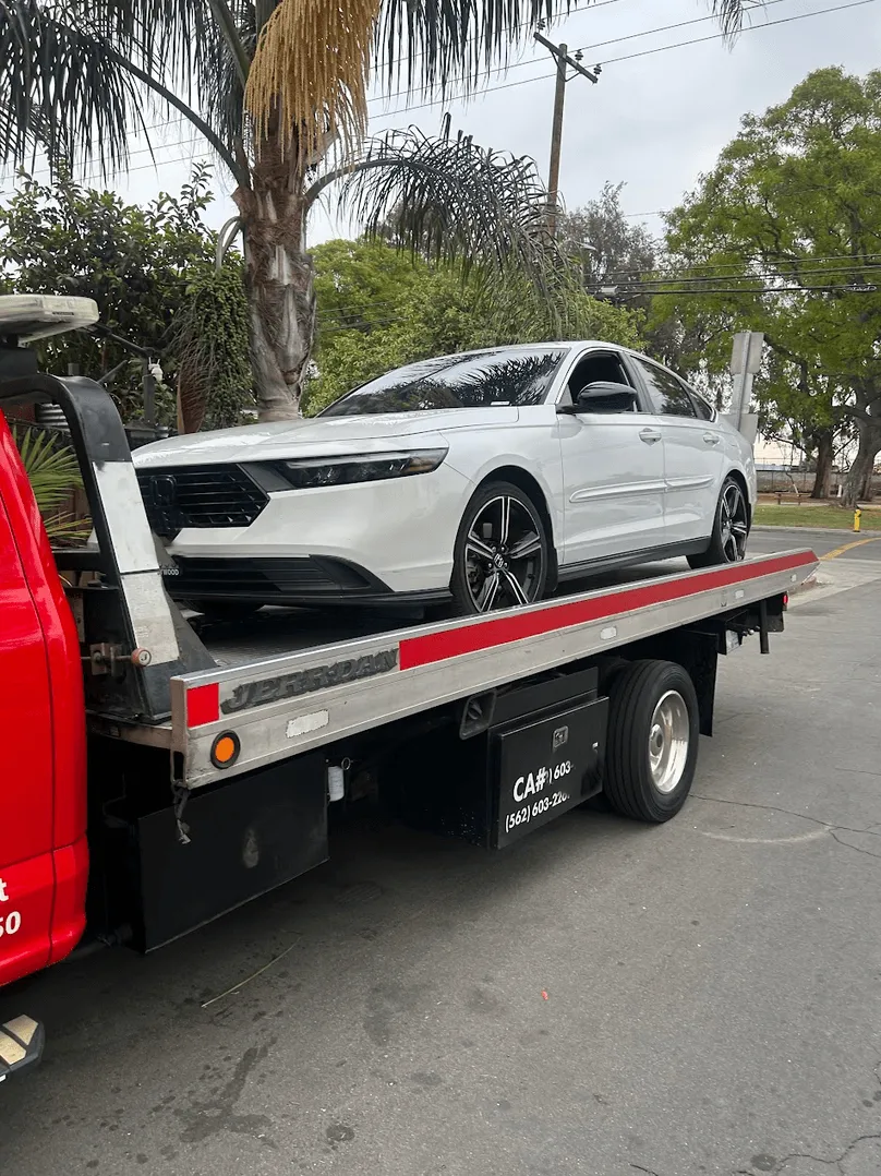 A white Honda sedan strapped onto a red Carsaad Towing flatbed on a residential street