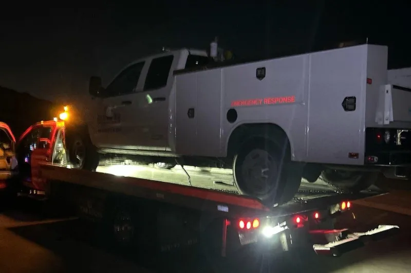 A white service truck loaded on a Carsaad Towing flatbed at night